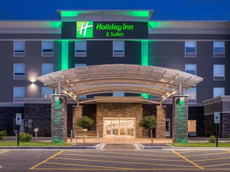 Exterior view of a Holiday Inn & Suites hotel at night with illuminated green sign and entrance canopy.