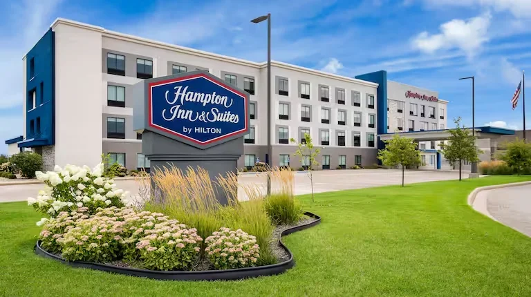 Exterior of Hampton Inn & Suites by Hilton hotel with a landscaped lawn and sign in front.