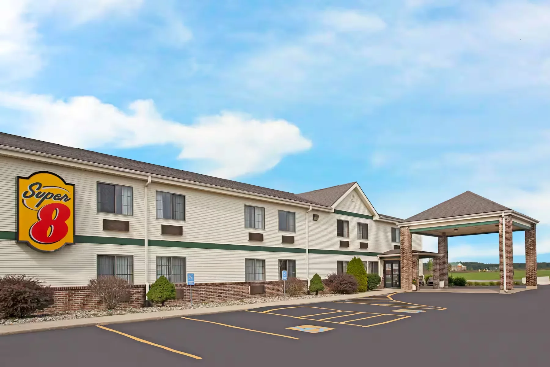Exterior view of a Super 8 motel with a large parking lot and designated handicapped parking spaces, under a partly cloudy blue sky.