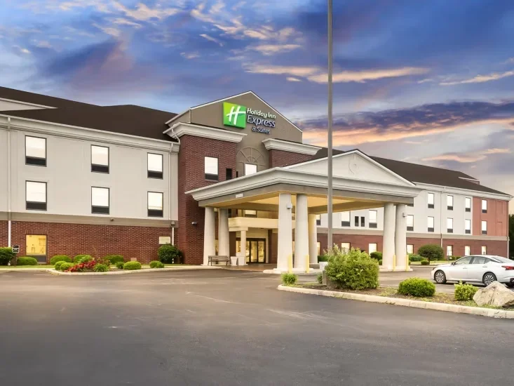 Exterior view of a Holiday Inn Express hotel during sunset, with the entrance, parking lot, and landscaping in view.