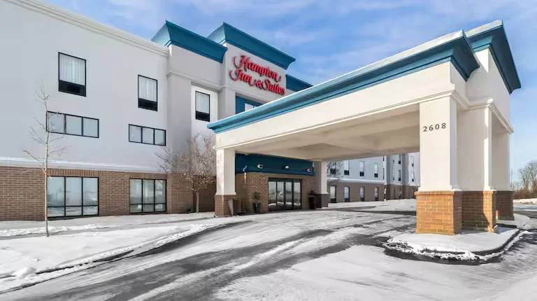 Exterior of Marriott TownePlace Suites hotel in snowy weather, showing white and blue building with a covered entrance, large sign, and snow-covered parking lot.