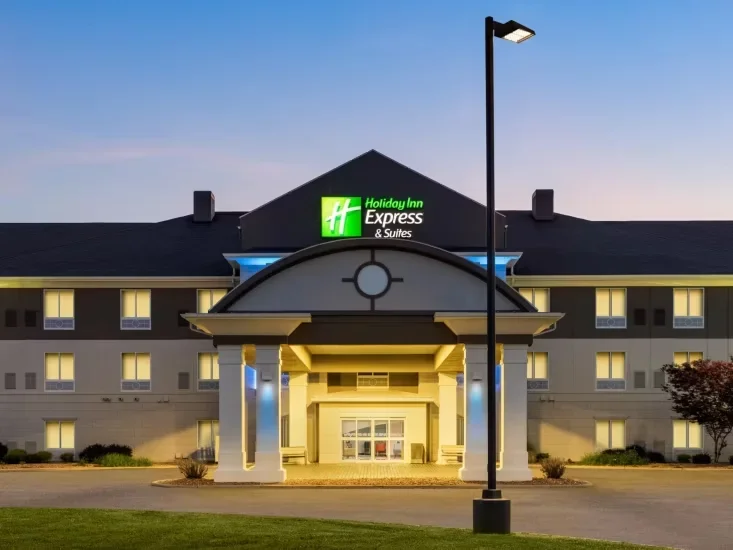 Front view of a Holiday Inn Express & Suites hotel at sunset, showing the entrance and illuminated signage.