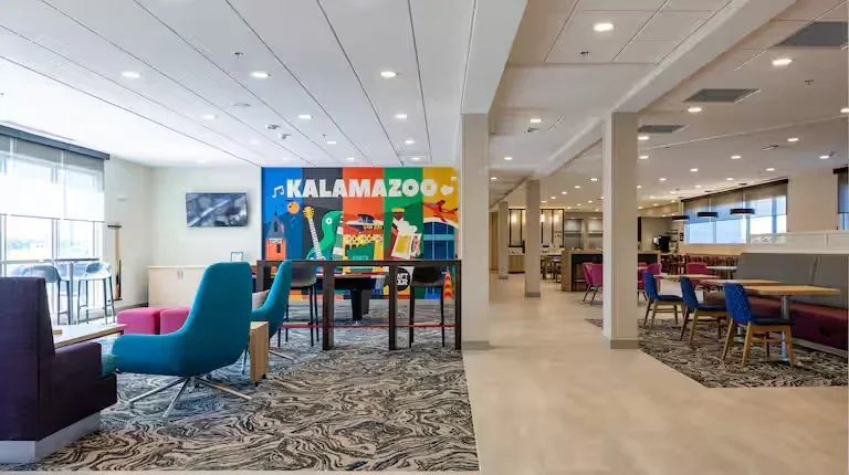 Interior of a modern lounge or waiting area with colorful furniture, a large Kalamazoo sign, and bright lighting.