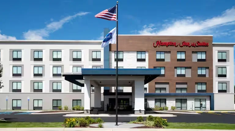 Hampton Inn & Suites hotel with an American flag and a hotel flag in front, on a sunny day with a blue sky.