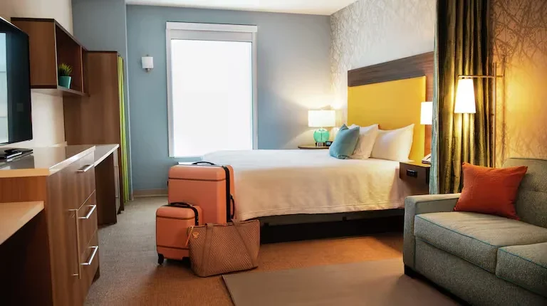Hotel room with bed, sofa, suitcase, and window.