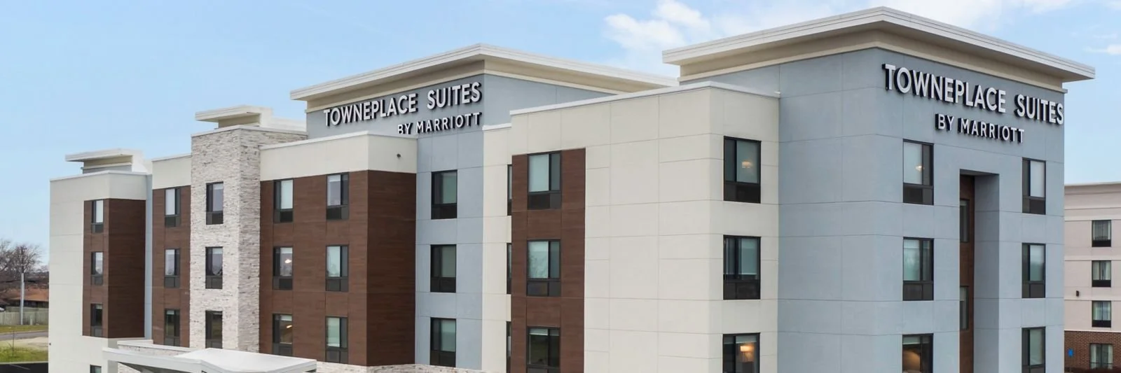 Exterior view of a modern five-story TownePlace Suites by Marriott hotel with a light-colored facade, multiple windows, and the hotel name, visible on the top of the building.
