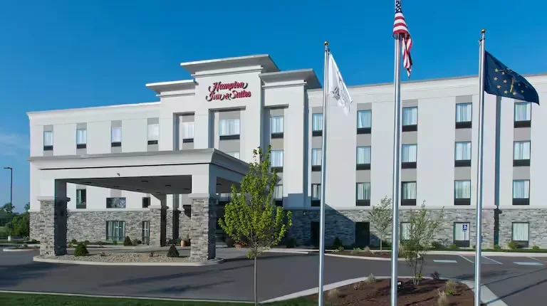 Exterior of a Hampton Inn & Suites hotel with flags in front, including the American flag, the Virginia state flag, and the European Union flag, under a clear blue sky.