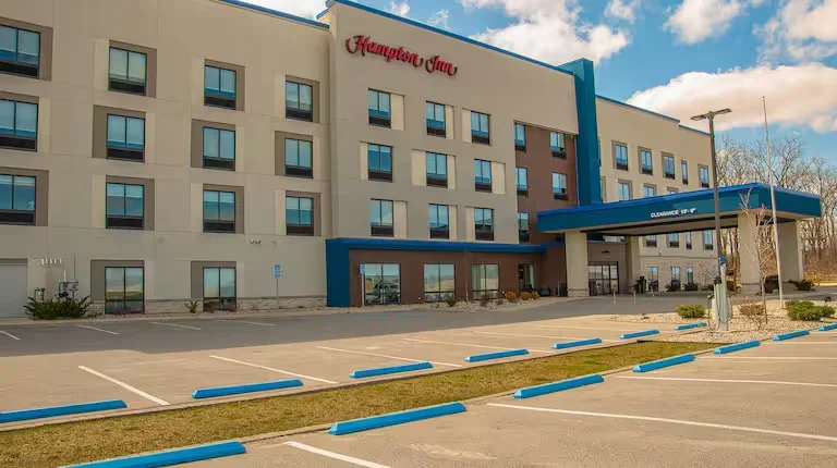 Exterior view of a Hampton Inn hotel with a parking lot in front and clear skies above.