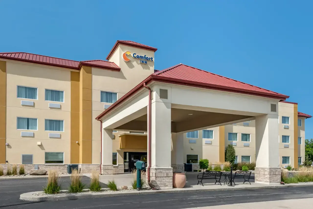 Comfort Inn hotel entrance with a covered drop-off area, benches, potted plants, and a clear blue sky.
