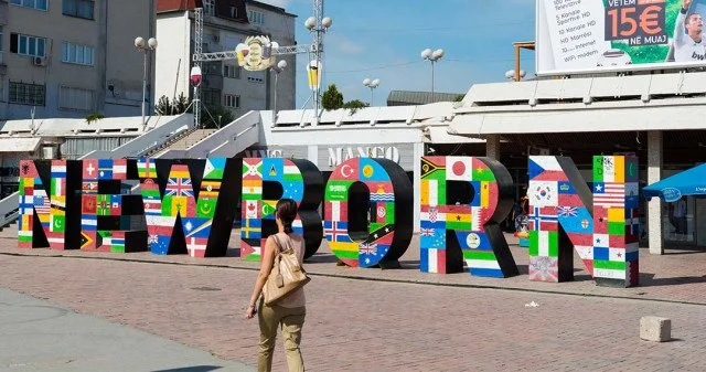 Großes Wort 'NEW BORN' aus Buchstaben mit Flaggen verschiedener europäischer Länder, im Freien mit einer Frau, die davor steht.