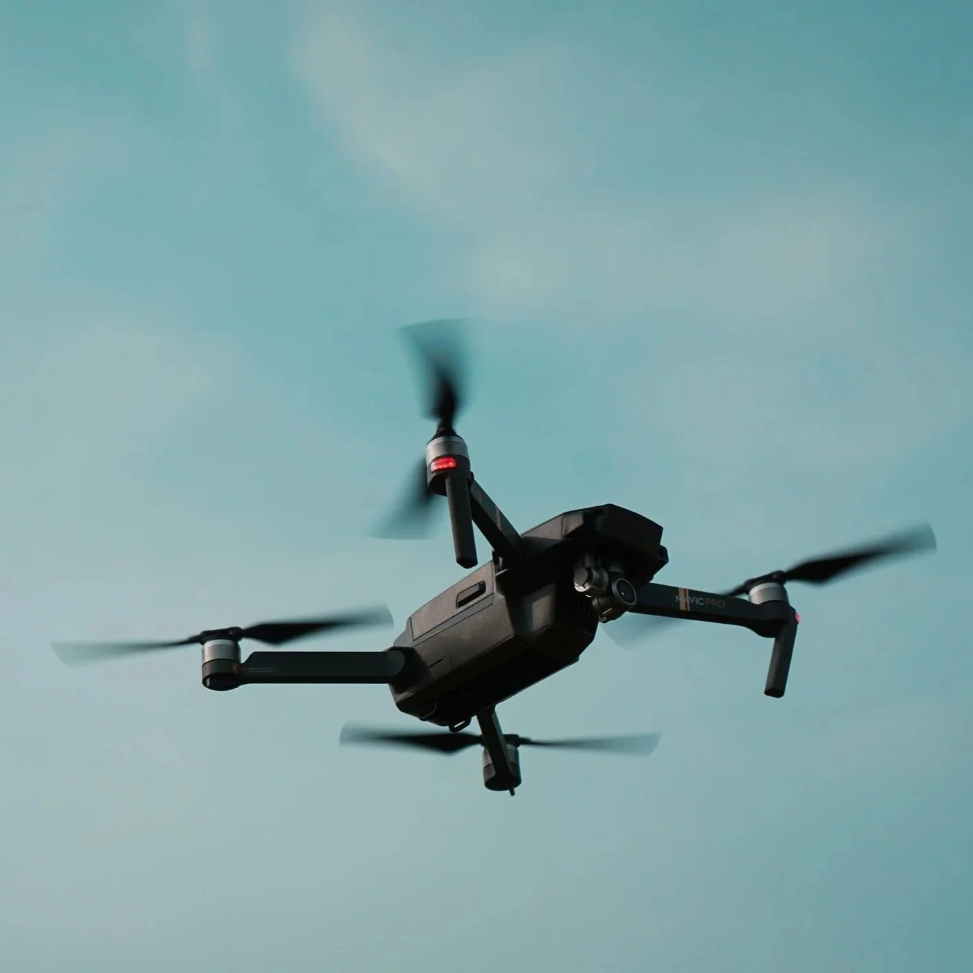 A black quadcopter drone flying in a clear sky.