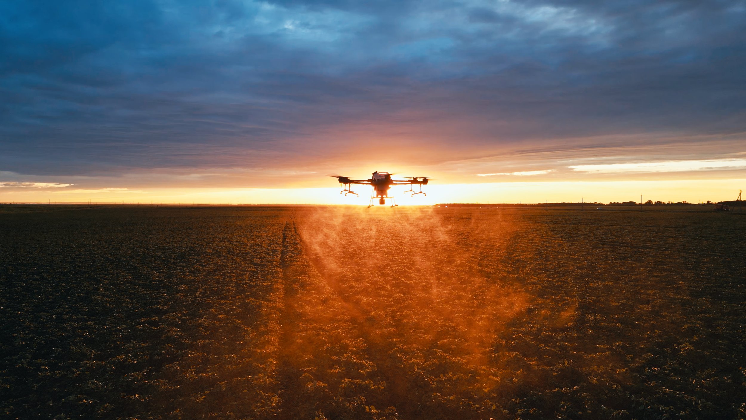 An drone flying over a field during sunset with a colorful sky.