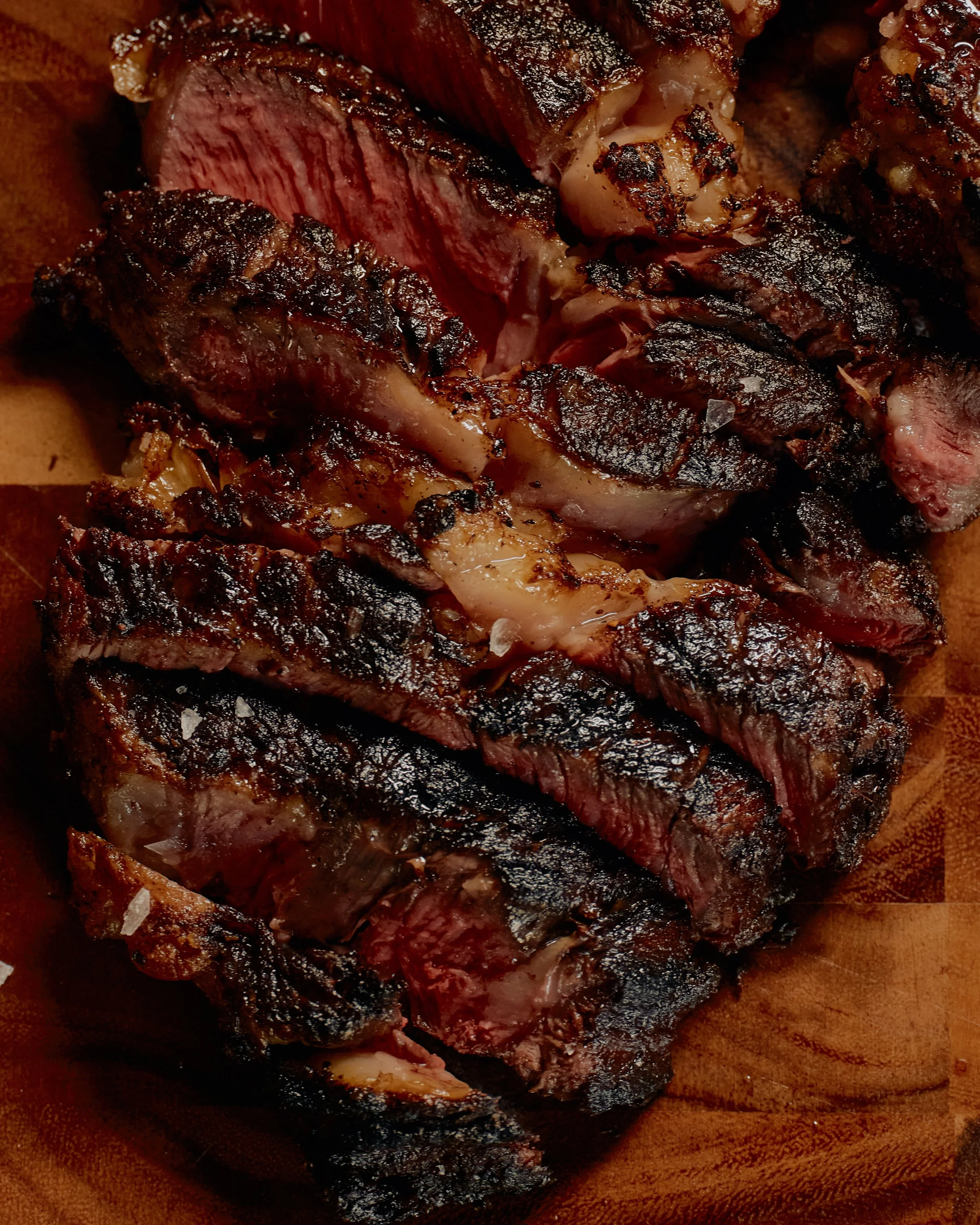 Close-up of a cooked steak with a dark, charred exterior and a pink interior, resting on a wooden surface.