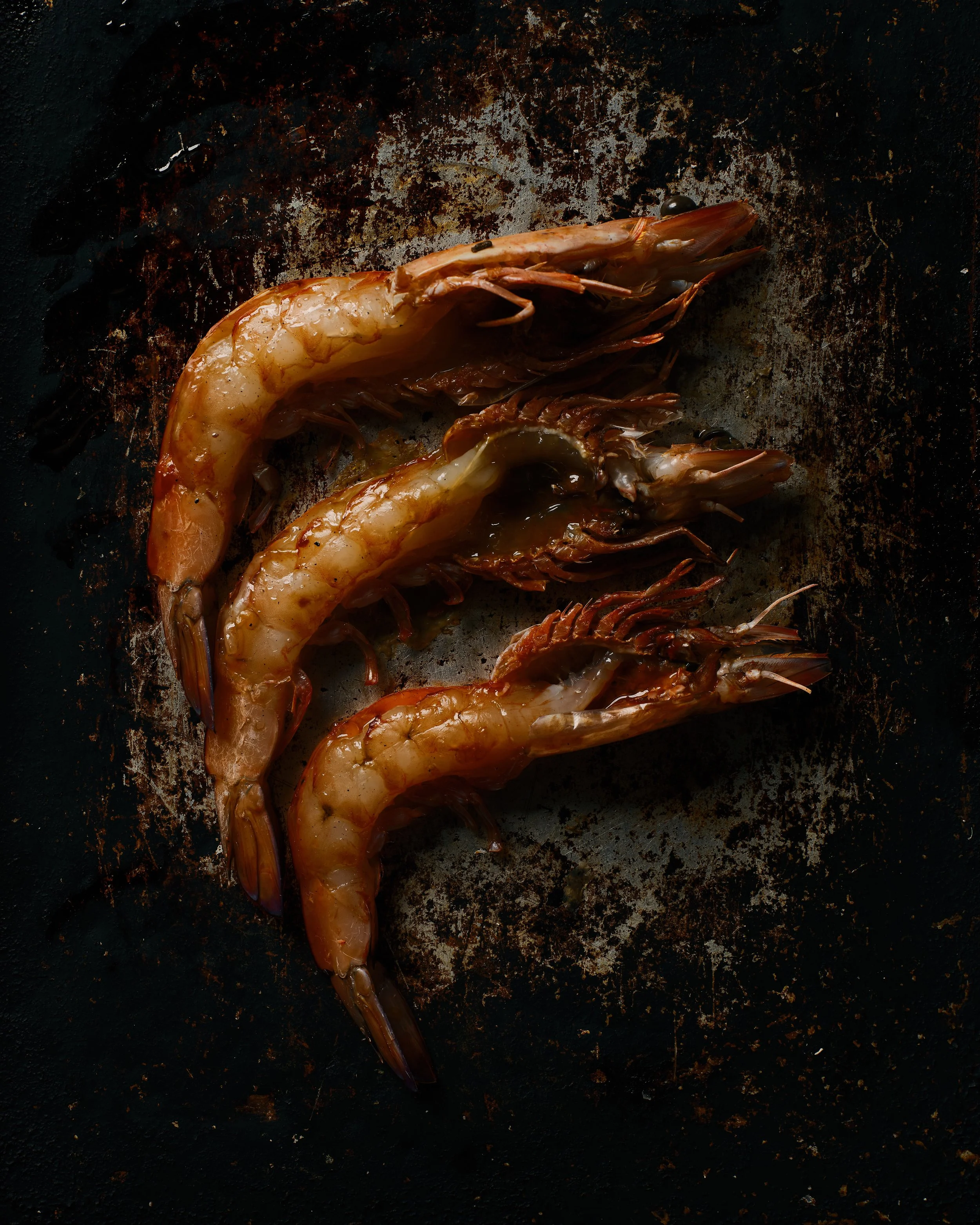 Raw shrimp on a dark, stained cooking surface.
