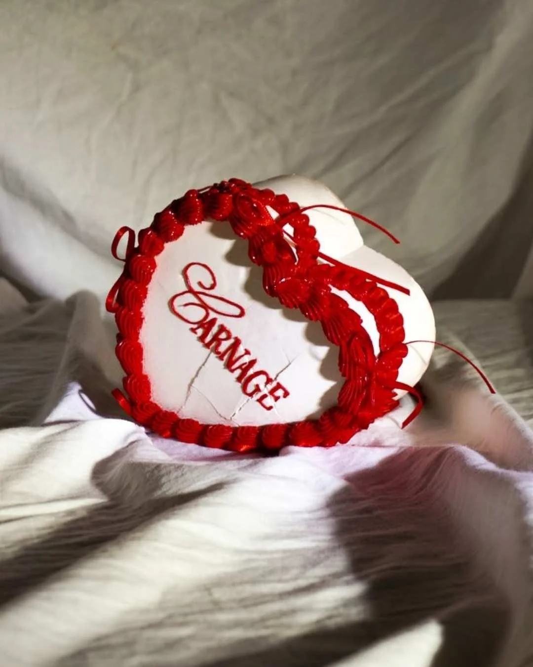 Cœur en céramique blanc avec inscription 'HARMAGE' en rouge, entouré d'une guirlande rouge, posé sur un tissu blanc.