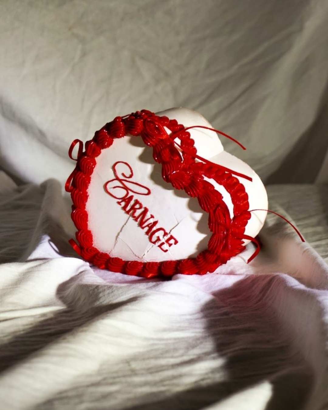 Coeur en pierre blanche avec écrit en rouge 'Valrange', entouré de rubans rouges, posé sur un tissu en lin blanc.