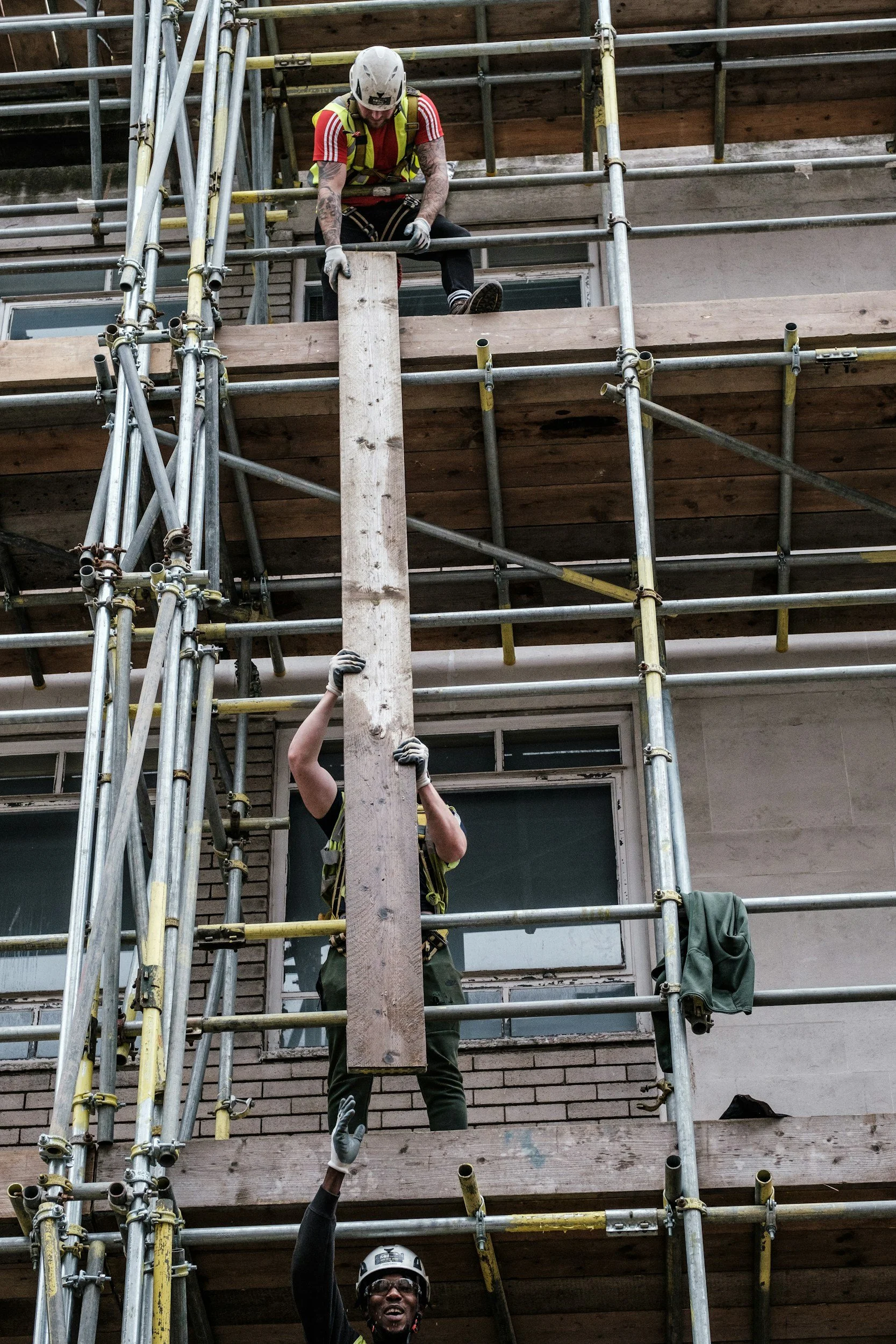 Construction workers wearing helmets and safety harnesses working on scaffolding outside a building.