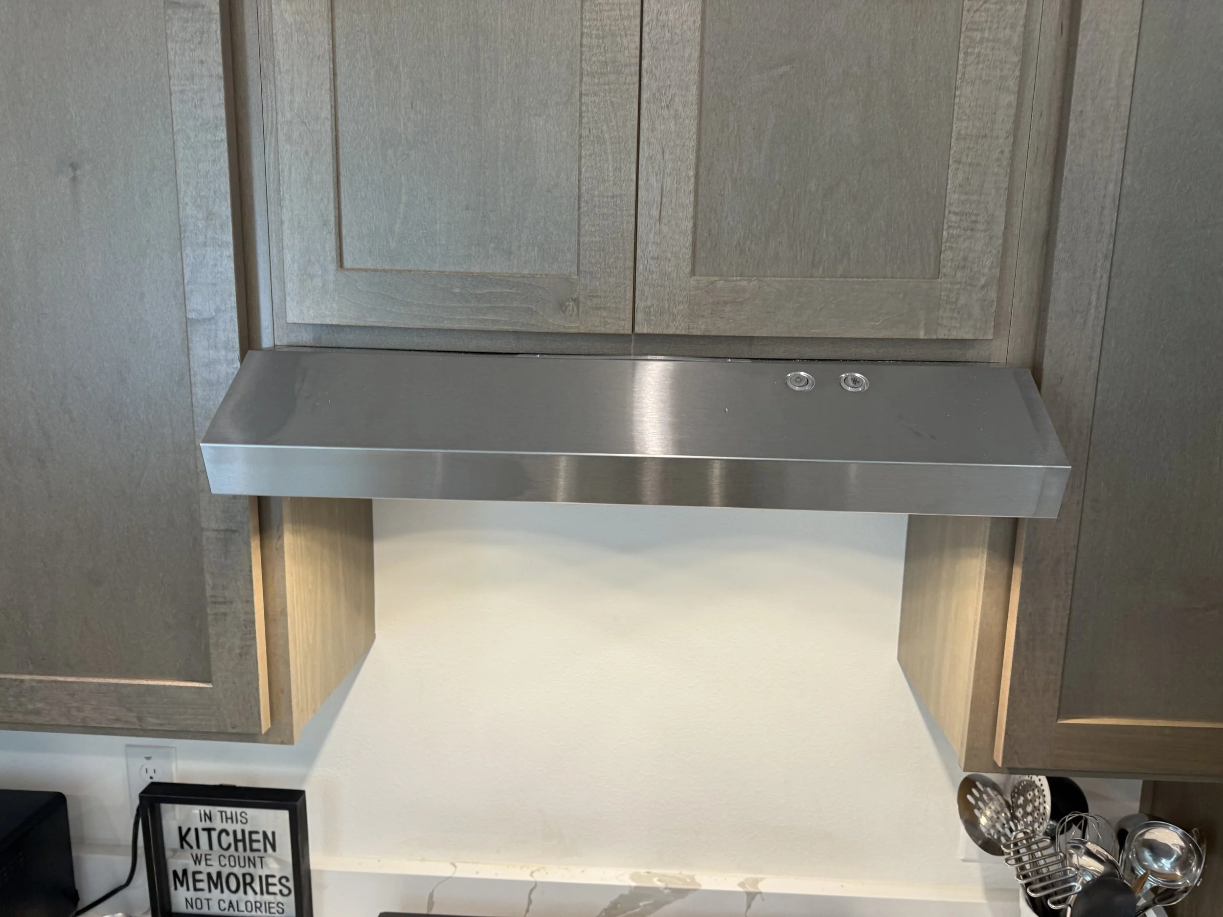 Kitchen area with wooden cabinets, a stainless steel appliance, and a framed sign on the counter that reads, "In this kitchen, we count memories, not calories."