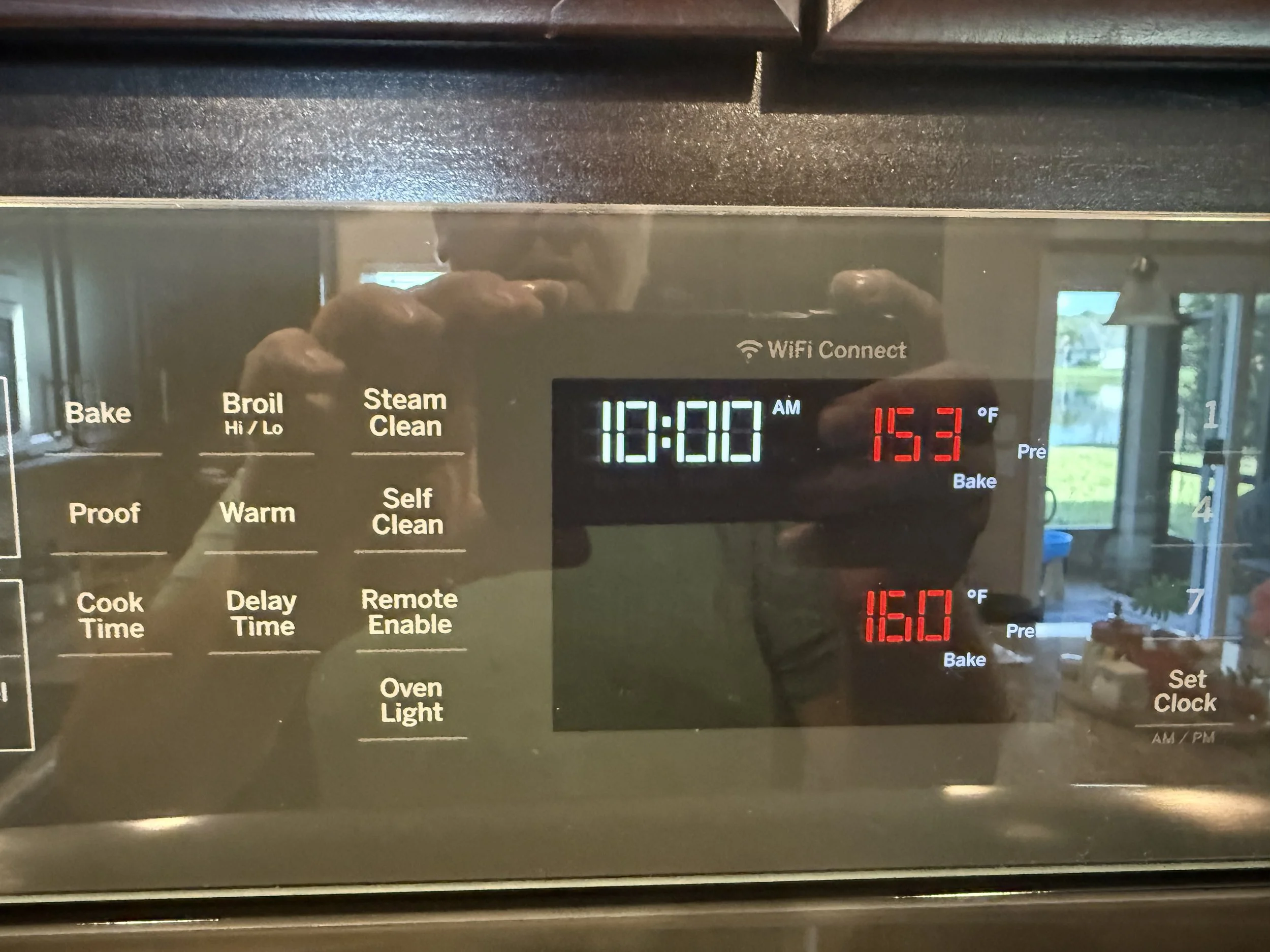 Close-up of a digital oven control panel showing the time 12:00 AM and a temperature of 165.1°F, with various buttons such as Bake, Broil, Steam Clean, Proof, Warm, Self Clean, and Oven Light.