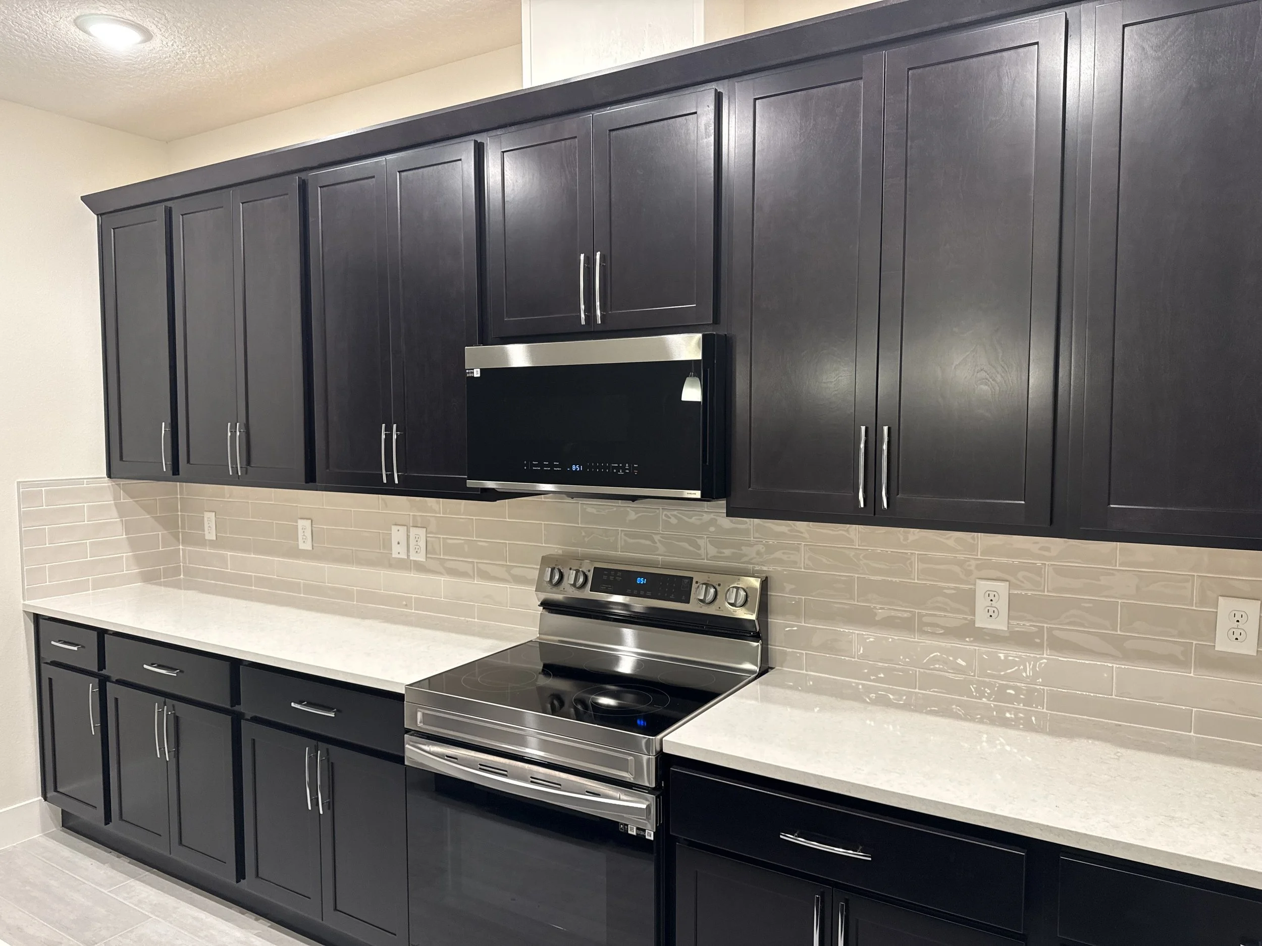 Kitchen with black cabinets, stainless steel microwave and stove, beige tile backsplash, and white countertops.