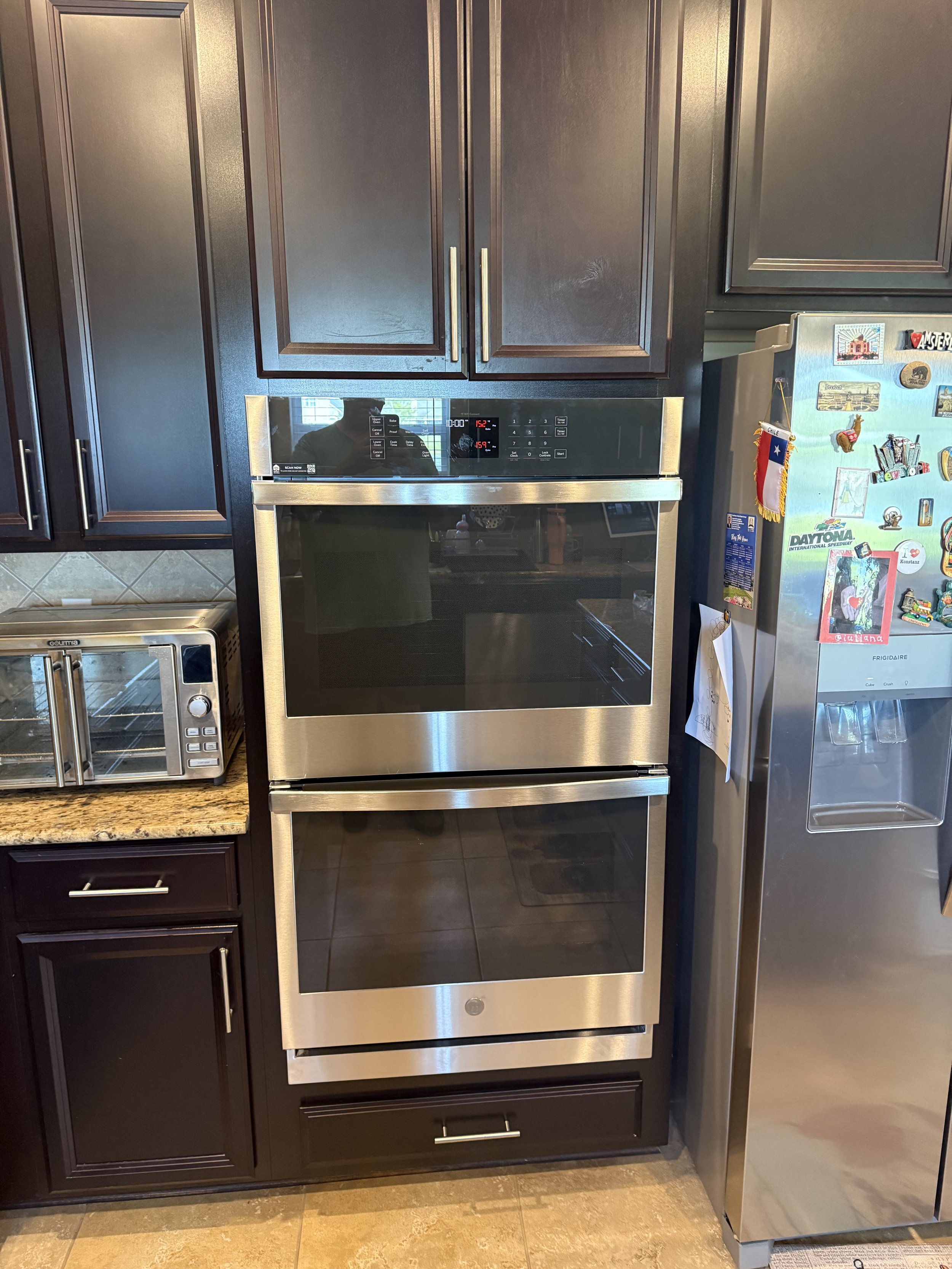 A kitchen with dark wood cabinets, a stainless steel oven, and a stainless steel refrigerator decorated with colorful magnets and souvenirs.