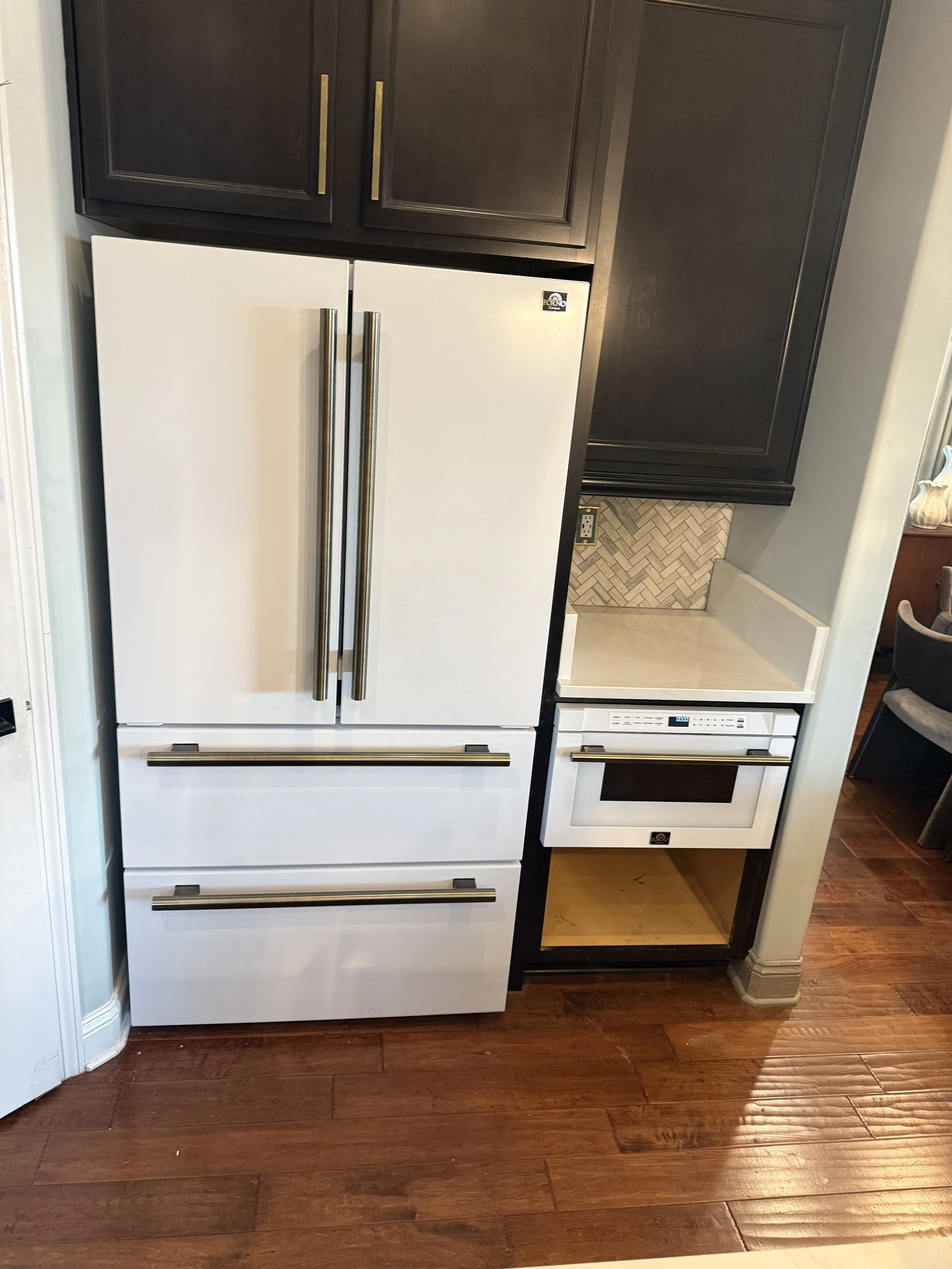 A white refrigerator with metallic handles, surrounded by dark brown kitchen cabinets, a decorative backsplash, and hardwood flooring.