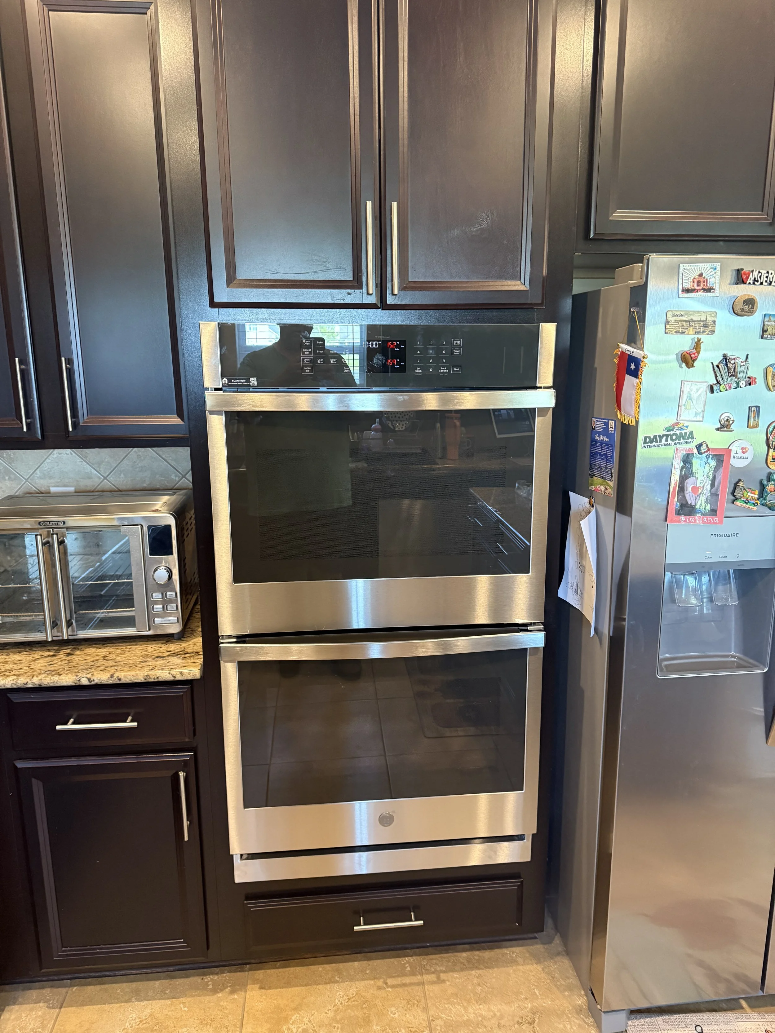 Modern kitchen with dark wood cabinets, stainless steel oven, and refrigerator decorated with colorful magnets and stickers.