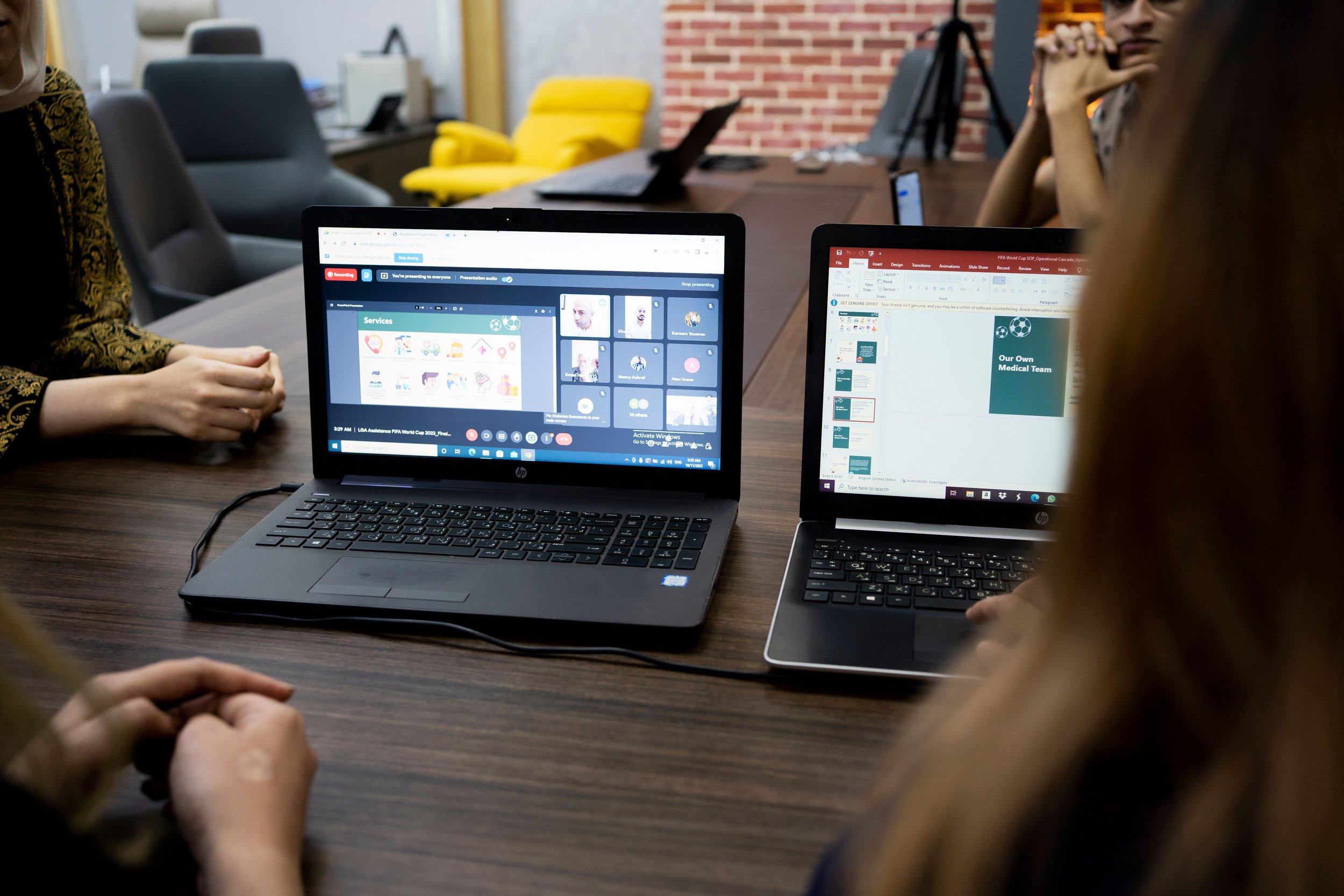 People sitting around a table with laptops open, participating in a virtual meeting or presentation in a conference room.