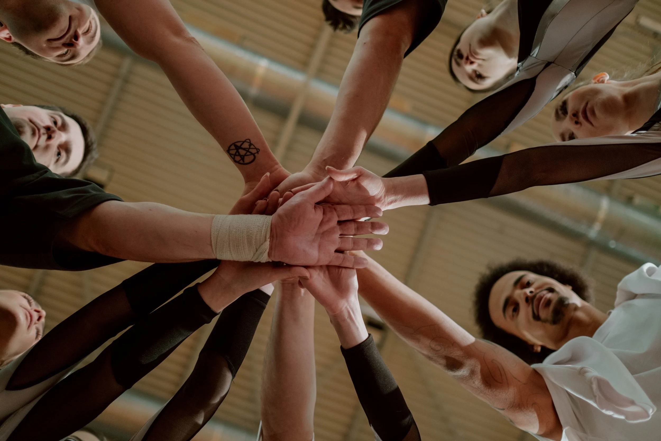 Group of diverse teammates with hanging arms stacked together in sports or team setting, showing unity and teamwork.