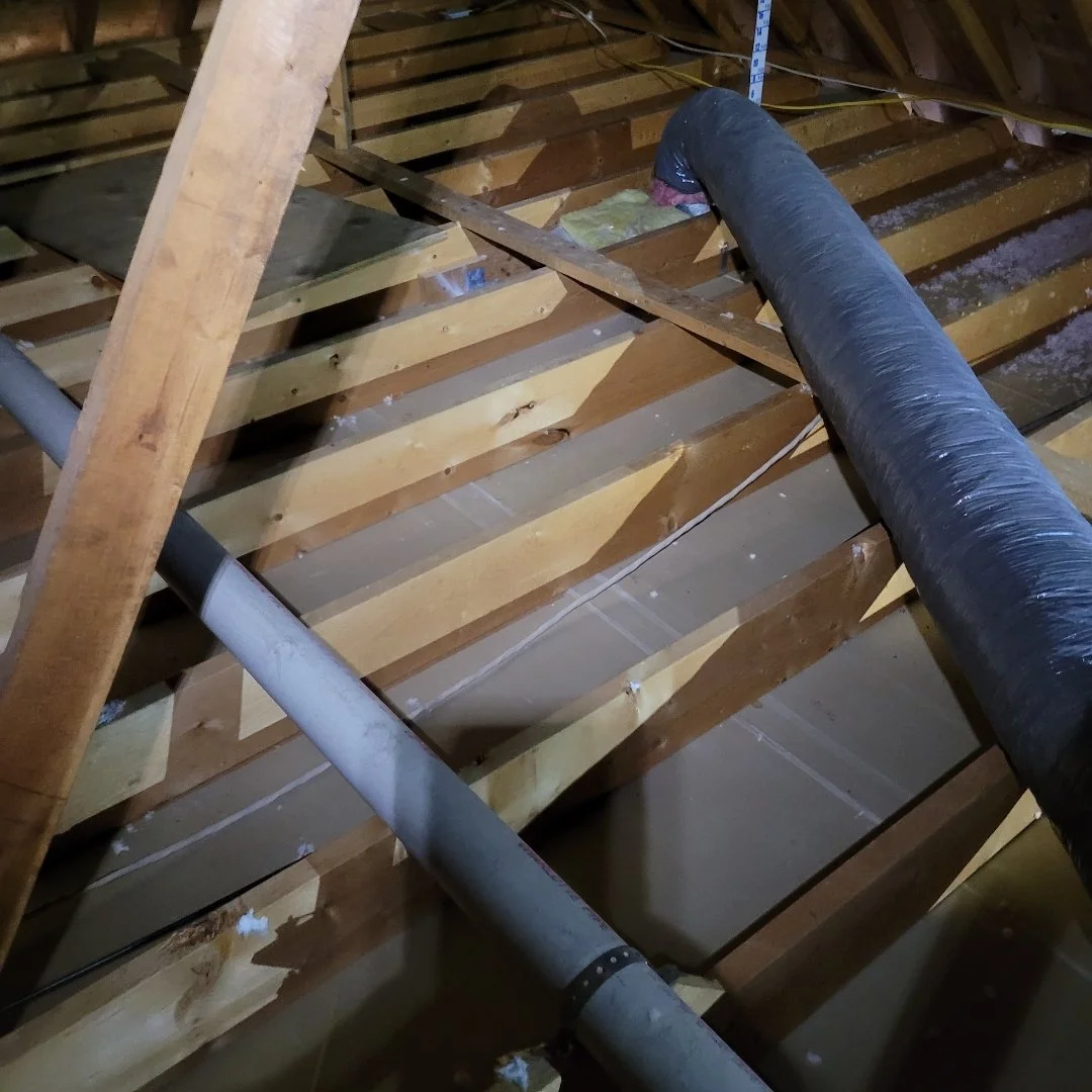 View of an attic showing exposed wooden floor joists, pipes, insulation, and ductwork.