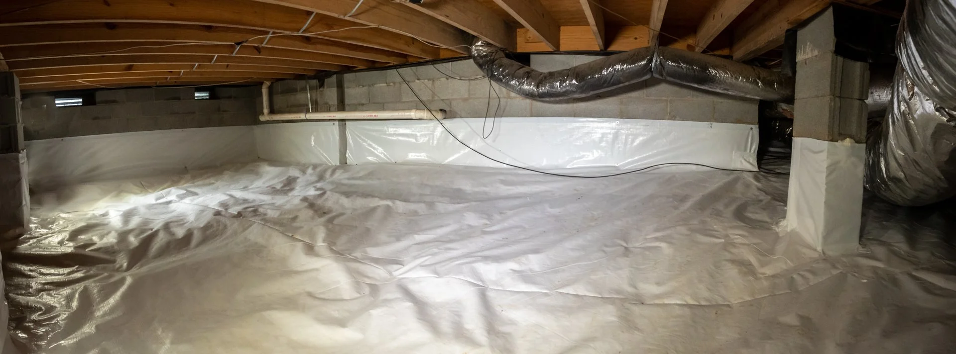 Basement with unfinished ceiling, insulation, and ductwork covered in plastic sheeting.
