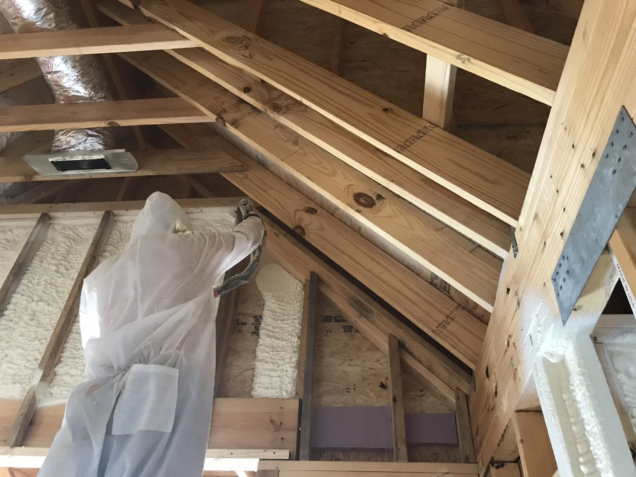 Interior view of a construction site showing wooden framing, insulation foam, and HVAC ductwork.