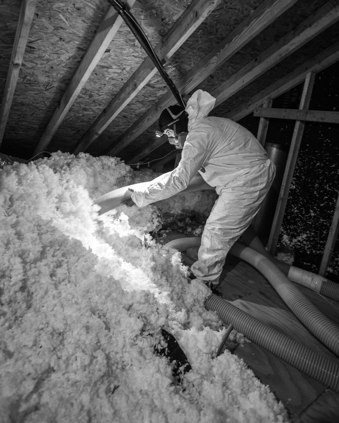 Insulation gets covered up the day it goes in, and nobody looks at it again. So we're going to show you. This is old loose fill coming out of an attic. Full Tyvek coverall, full-face respirator with pink cartridges, and a vacuum hose worked down into