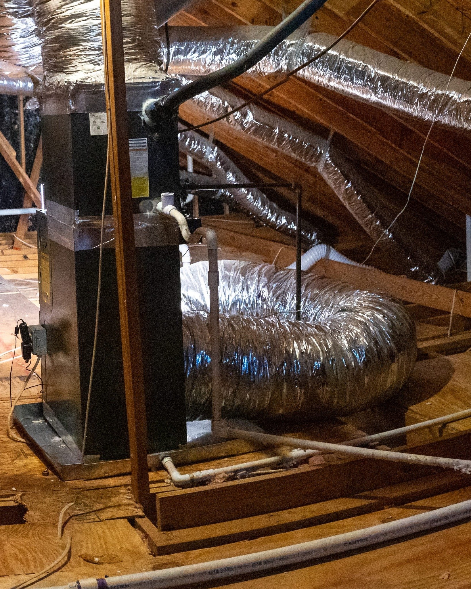 Removal is its own scope of work. Slide one is an attic cleared down to the joists, wiring and a metal pipe showing across the deck, a black air handler with foil ducts running off it. Slide two is what the same attic looked like before anybody touch