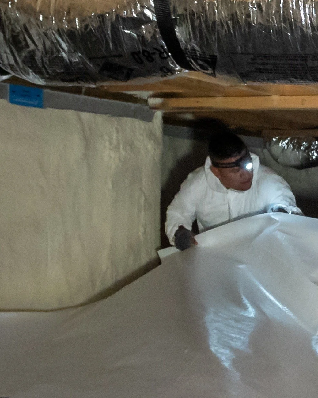 Last phase of the install. We start at the back of the crawl space and work our way out. Clean white poly over a foamed wall, every seam and edge bonded down with double-sided tape. The blue tag on the wall is the termite inspection record, and it st