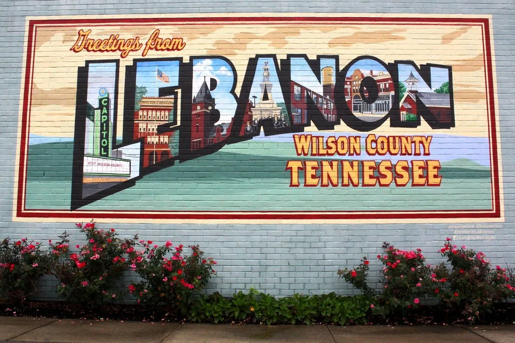 Colorful mural on a brick wall promoting Lebanon, Wilson County, Tennessee, with images of local landmarks inside the large text 'Lebanon' and flowers in front.