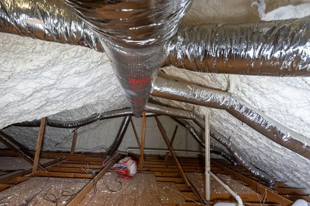 Attic space with ductwork, insulation spray foam, and wooden floor joists.