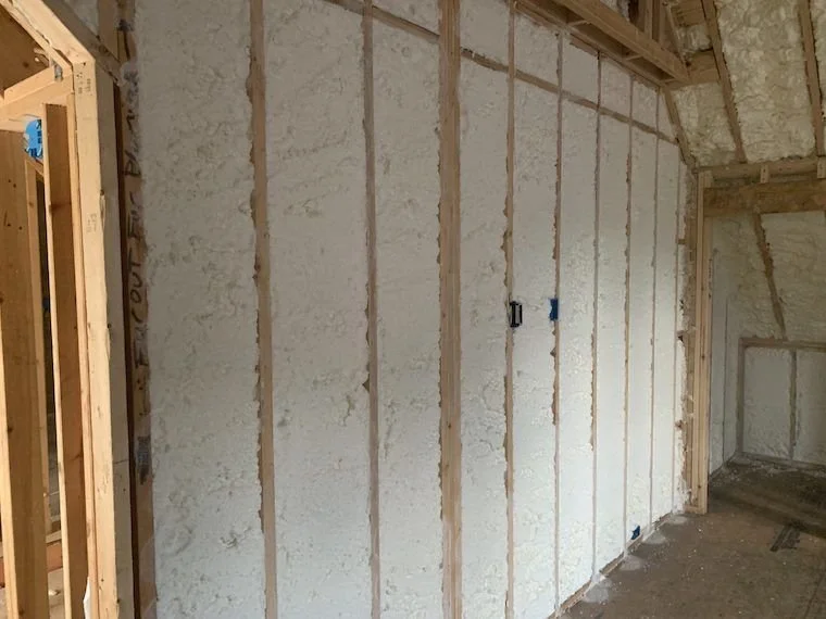 Interior of a building under construction with wooden studs and spray foam insulation on the walls.