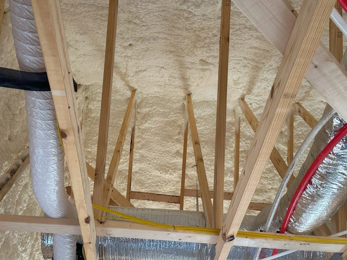 View of a building's ceiling with wooden framing, spray foam insulation, and air ducts.