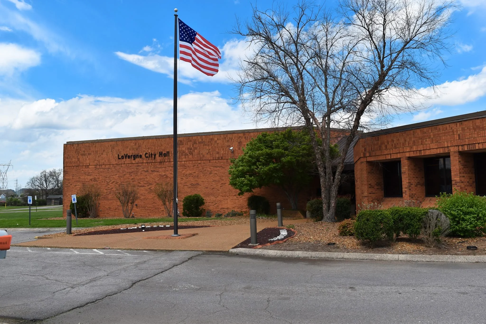American flag flying in front of LaVergne City Hall building with trees and parking lot in the foreground.