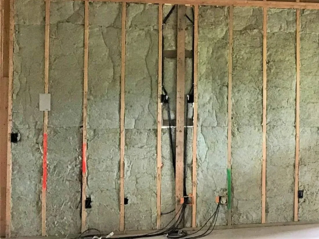 Interior of a wall with wooden studs and insulation, with electrical wiring and outlets installed.