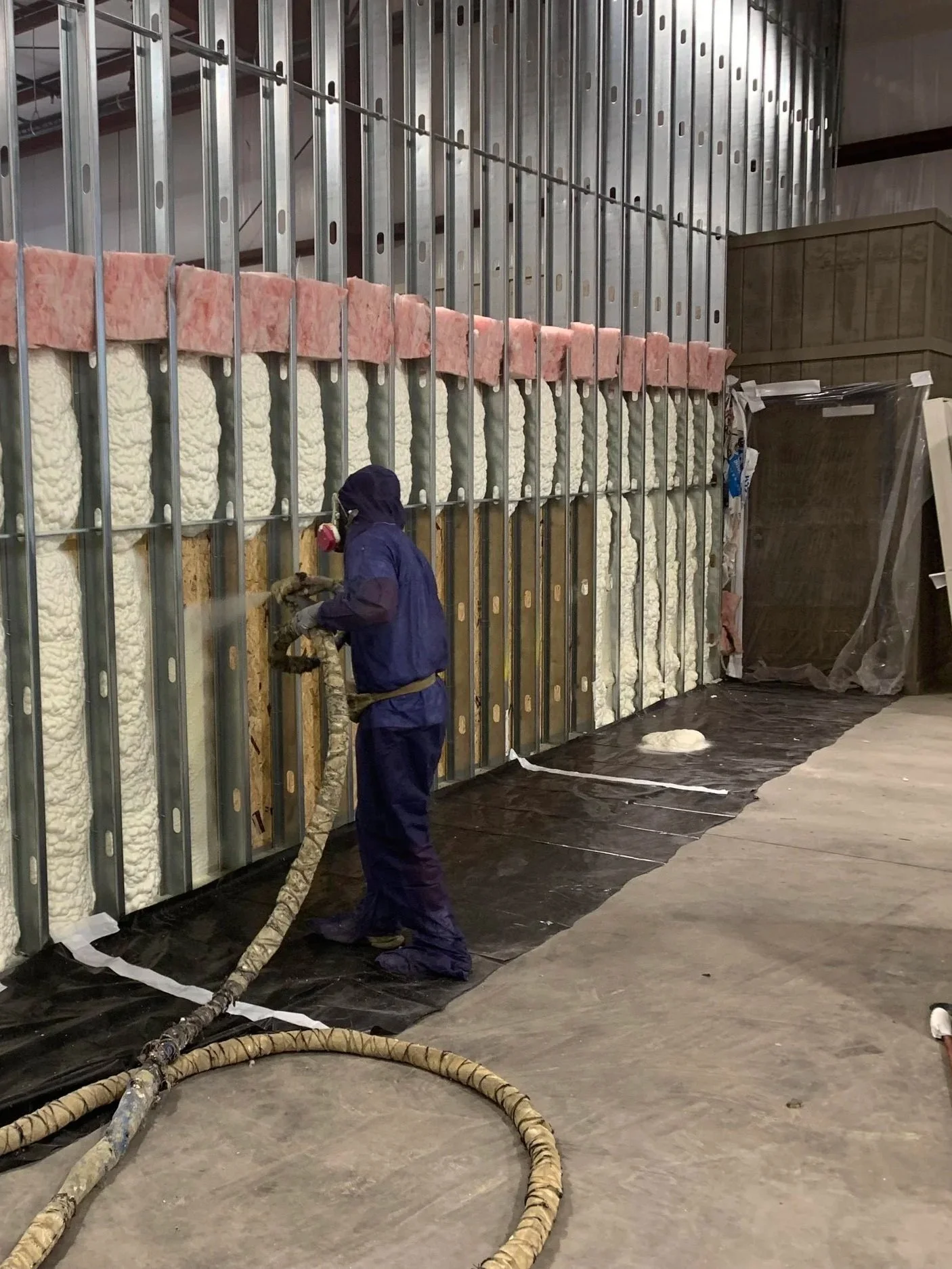 Worker wearing protective gear using industrial equipment to insulate or install spray foam insulation in a building under construction.