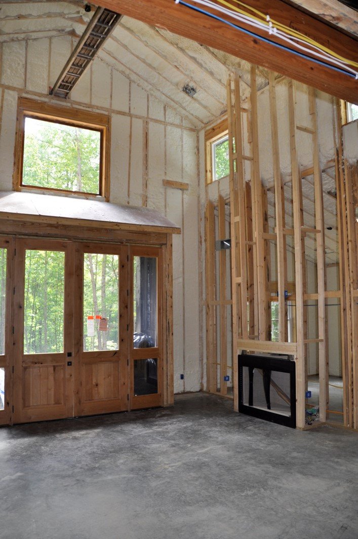 Interior of a house under construction with exposed framing, large windows, and open wall spaces.