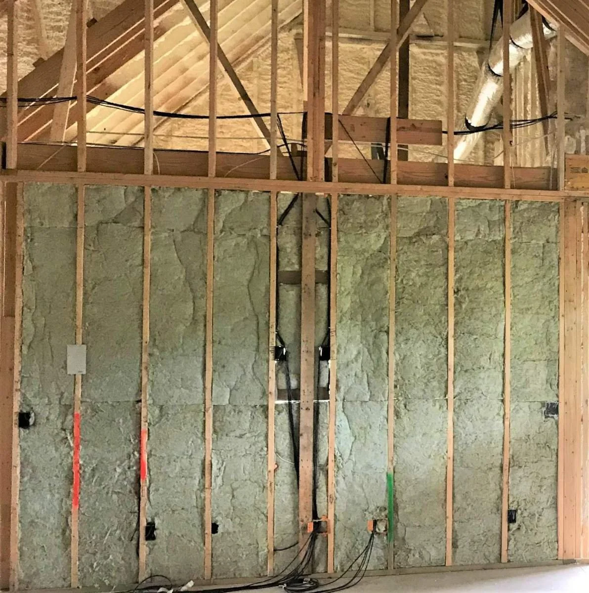 Interior wall under construction with wooden framing and insulation, electrical wiring, and ductwork visible.