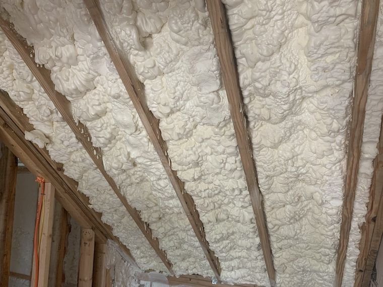 Insulation foam sprayed between wooden ceiling beams in a room under construction.