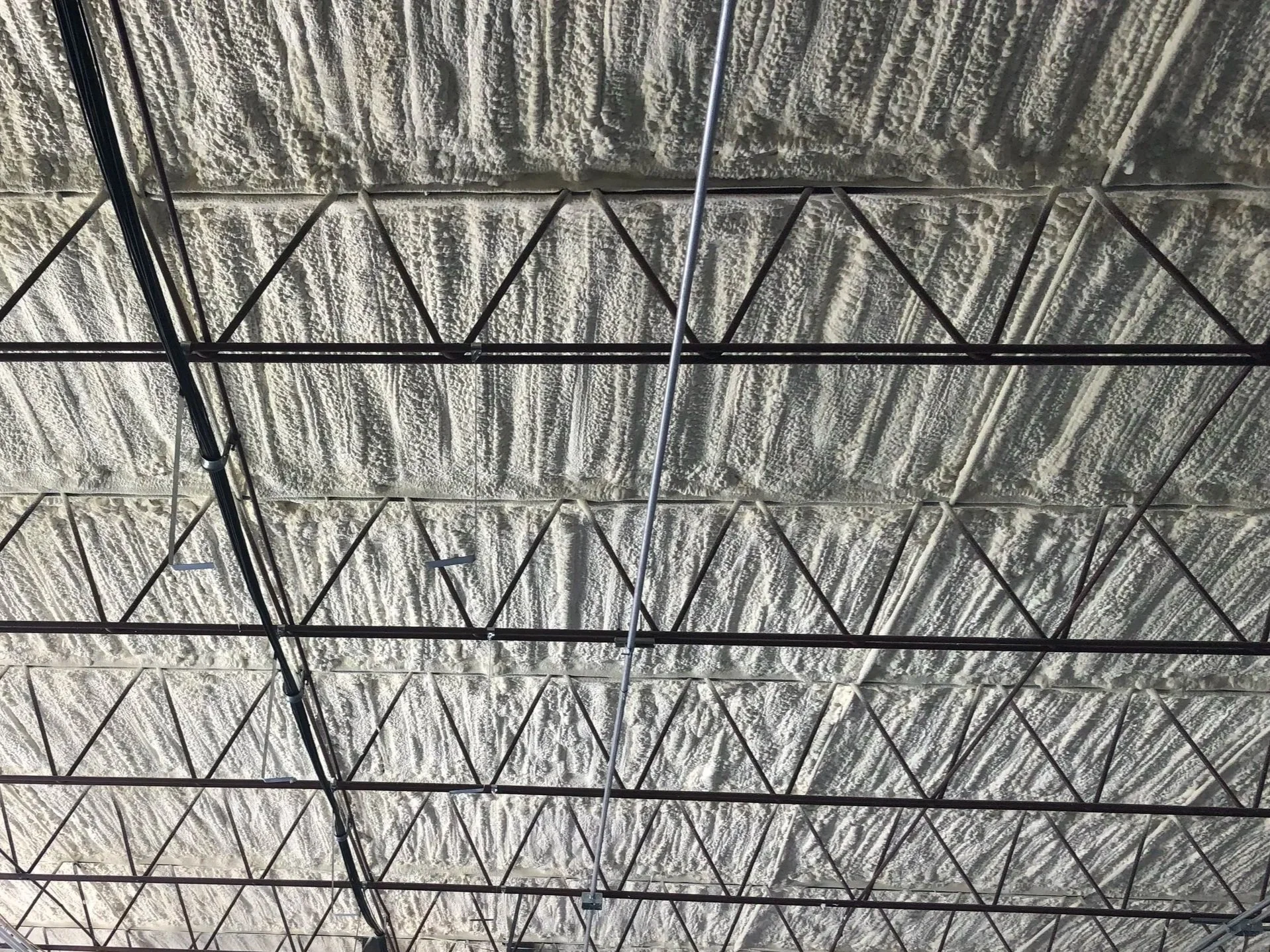 Ceiling of an industrial building with exposed insulation, metal beams, and lighting fixtures.