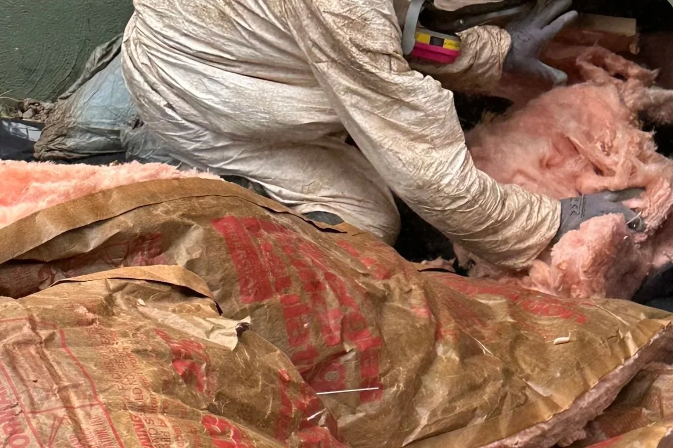 Person wearing personal protective wear removing old insulation from crawl space.