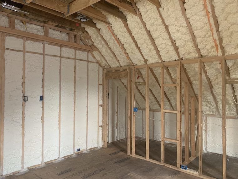 Interior of a house under construction with wooden framing and spray foam insulation on the walls and ceiling.
