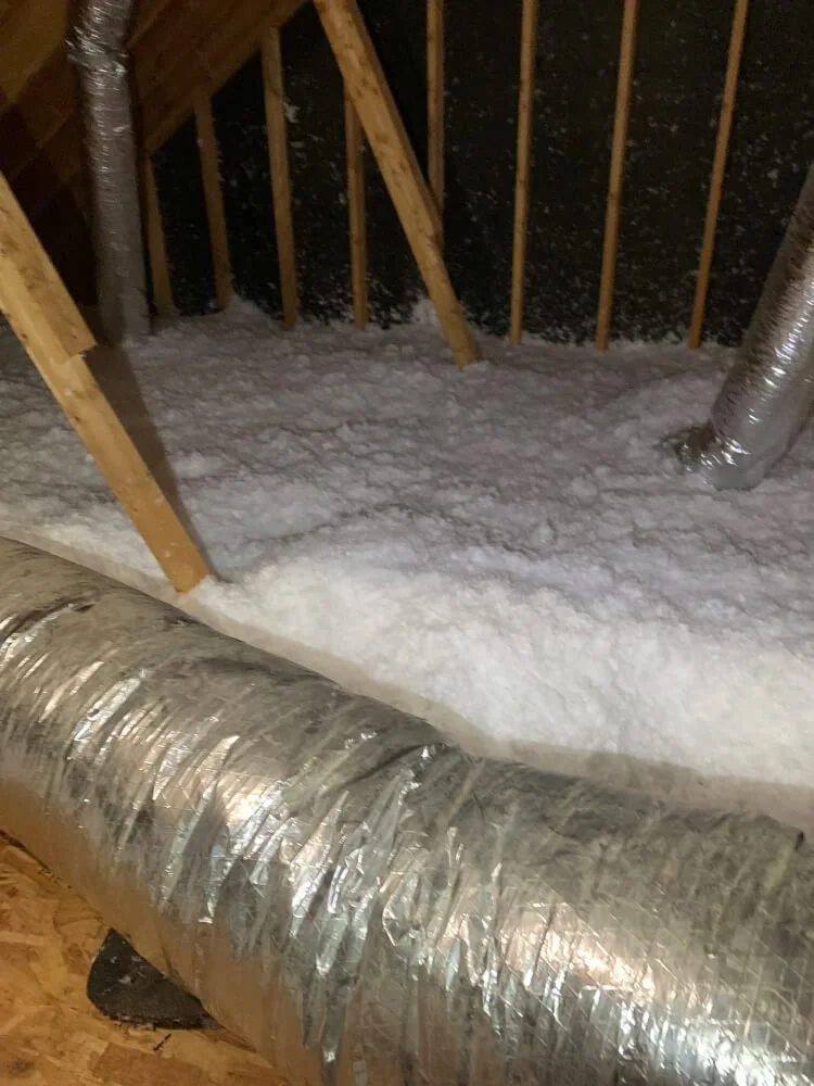 Insulation inside an attic with exposed wooden beams and ductwork.