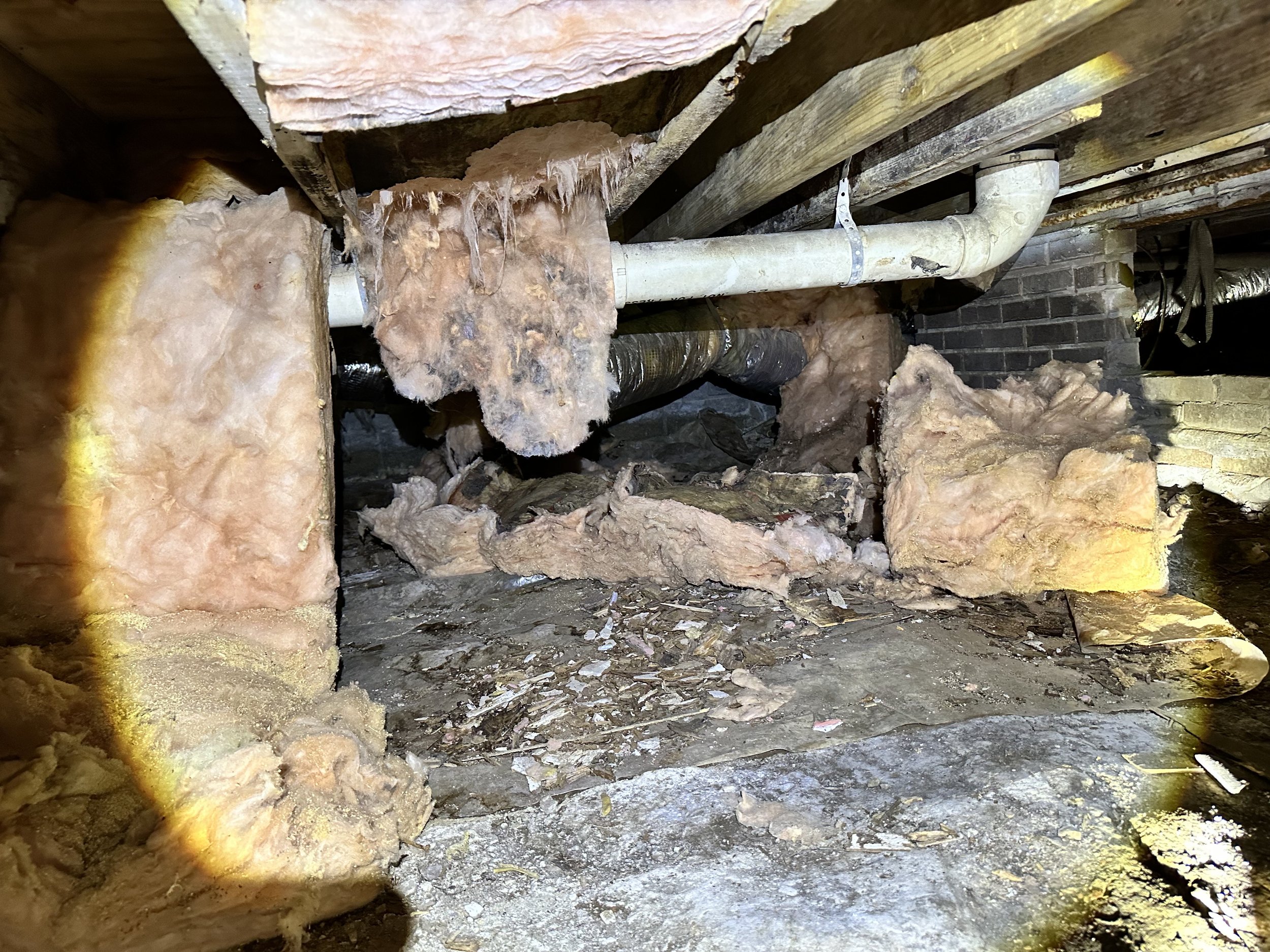 Photo showing an the crawl space of a home with old and dirty insulation